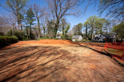 Cleared residential lot with exposed red clay soil in established neighborhood
