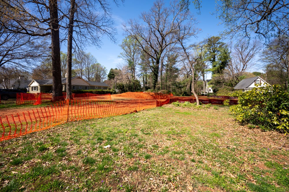 Vacant residential lot with orange safety fencing and mature trees in established neighborhood