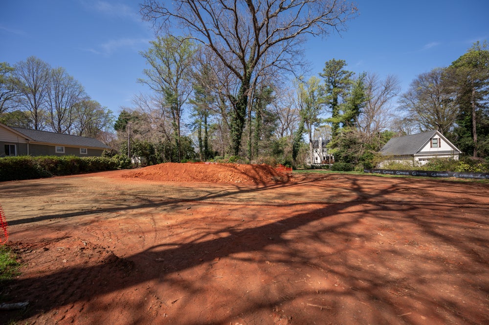 Vacant residential lot with cleared red clay soil in established neighborhood