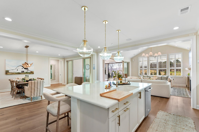 Open-concept kitchen with white island, quartz countertops, and pendant lights, flowing into dining and living areas with hardwood floors.