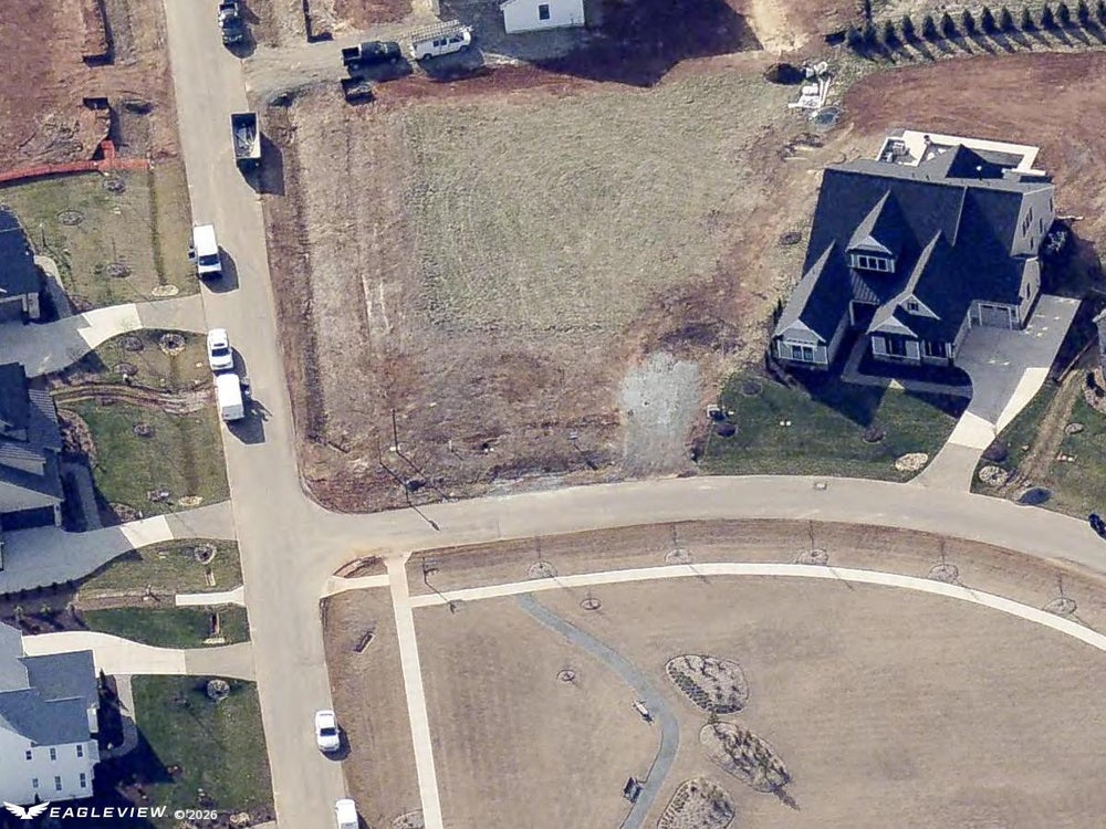 Aerial view of vacant residential lot in subdivision with paved streets and nearby homes