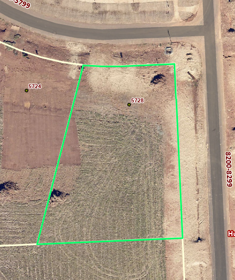 Aerial view of vacant residential lot outlined in green with adjacent paved roads