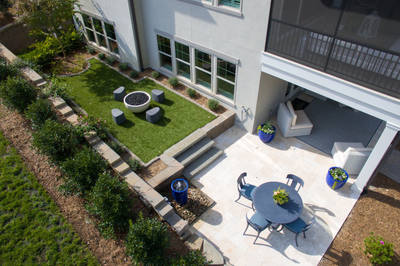Aerial view of backyard patio with dining set, fire pit on grass lawn, and covered seating area beside two-story home.