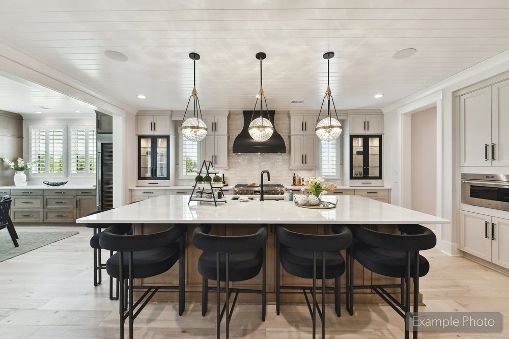 Large kitchen island with white countertop, black barstools, and three pendant lights above