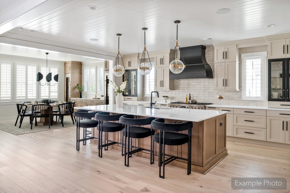 Open kitchen with large wood island, black barstools, pendant lights, and cream cabinets, open to dining area