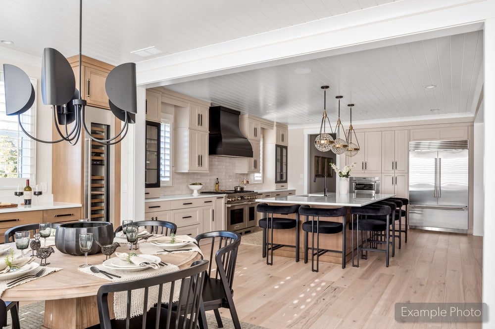 Open-concept kitchen and dining area with large island, black barstools, light wood floors, and stainless steel appliances