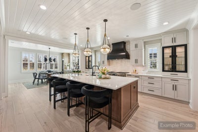 Open kitchen with large wood island, white cabinets, black range hood, and pendant lights over bar seating