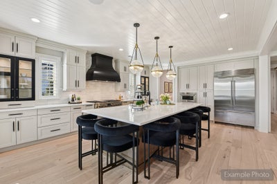 Large kitchen with white cabinets, center island with black barstools, black range hood, and stainless steel appliances
