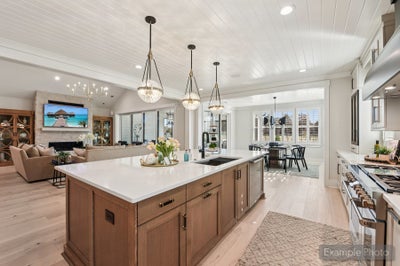 Open-concept kitchen with large wood island, white countertops, pendant lights, and view into living and dining areas