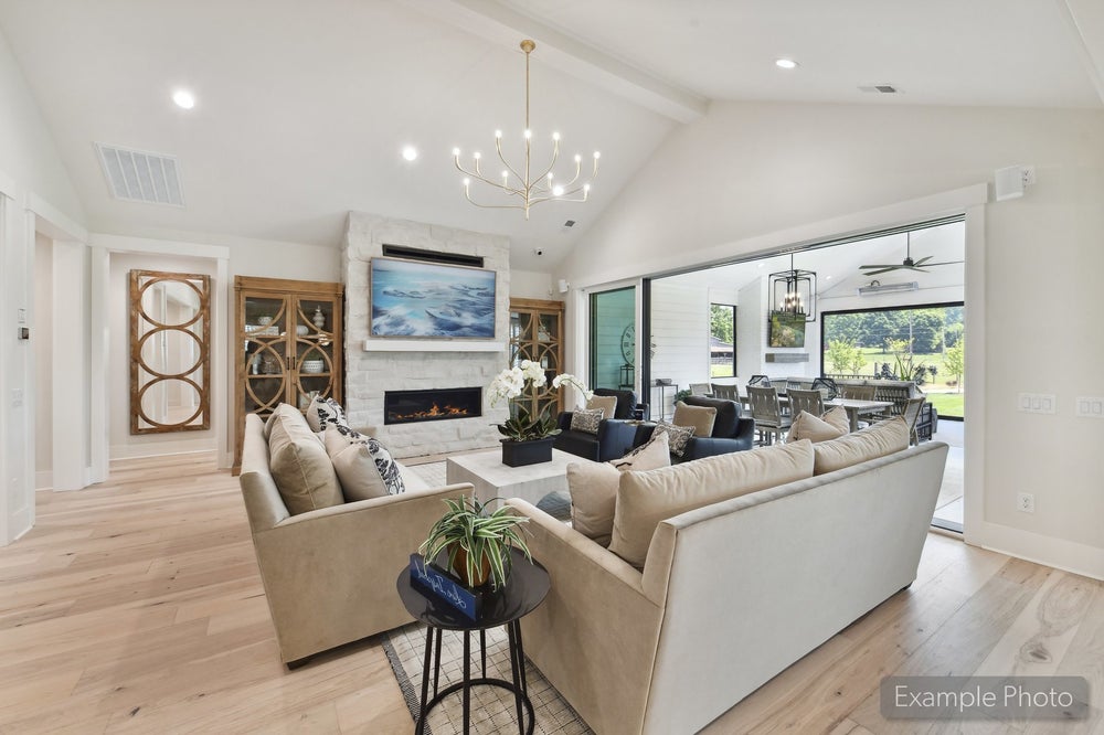 Open living room with vaulted ceiling, stone fireplace, hardwood floors, and sliding doors to outdoor patio