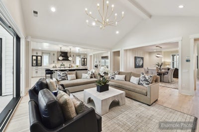 Open-concept living room with vaulted ceiling, chandelier, and kitchen visible in background