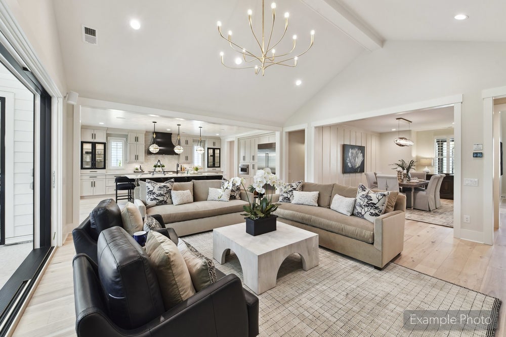 Open-concept living room with vaulted ceiling, chandelier, and kitchen visible in background