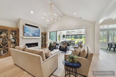 Open living room with vaulted ceiling, stone fireplace, hardwood floors, and sliding doors to covered patio