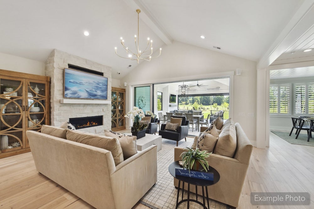 Open living room with vaulted ceiling, stone fireplace, hardwood floors, and sliding doors to covered patio