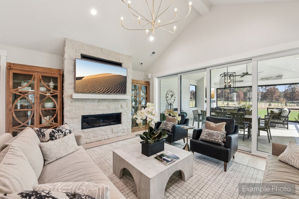 Living room with vaulted ceiling, stone fireplace, wall-mounted TV, and sliding glass doors to outdoor patio