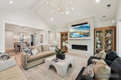 Living room with vaulted ceiling, stone fireplace, wall-mounted TV, and gold chandelier, open to dining area