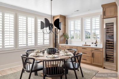 Dining area with round table, black chairs, wood cabinetry, wine fridge, and plantation shutters on multiple windows