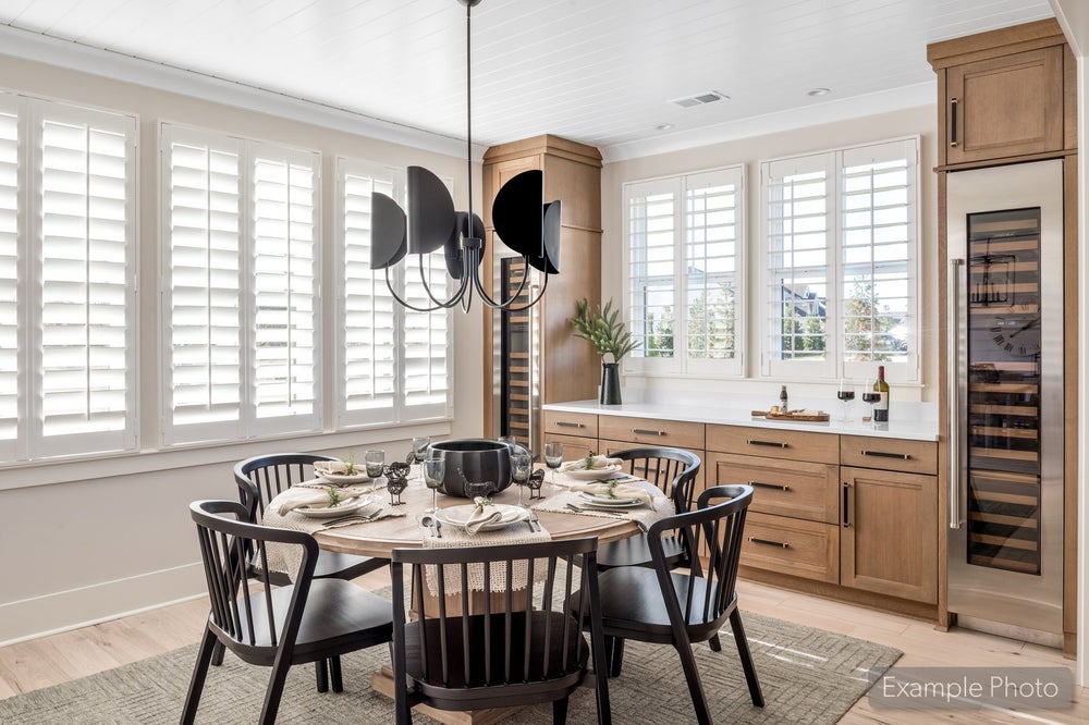 Dining area with round table, black chairs, wood cabinetry, wine fridge, and plantation shutters on multiple windows