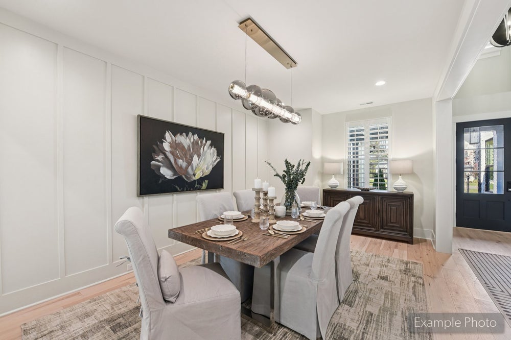 Dining room with wood table, upholstered chairs, board and batten walls, and modern pendant light fixture over hardwood floors