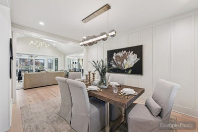 Dining room with wood table, upholstered chairs, pendant light, and white panel walls open to living area