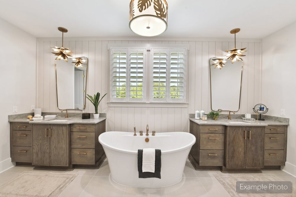 Master bathroom with freestanding soaking tub, dual wood vanities, gold fixtures, and plantation shutters