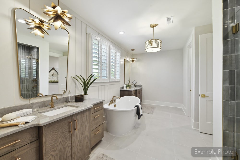 Master bathroom with freestanding soaking tub, dual vanity with marble countertops, and gold fixtures