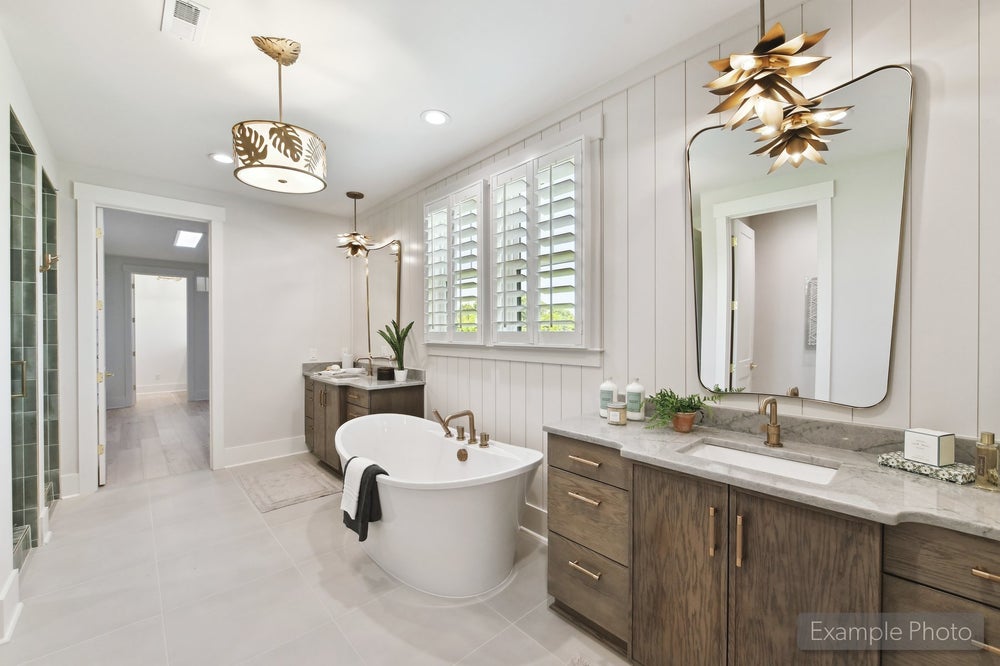 Master bathroom with freestanding soaking tub, dual wood vanities, marble countertops, and decorative gold pendant lights