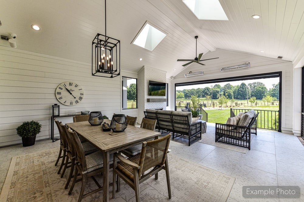 Covered outdoor living area with dining table, seating, vaulted shiplap ceiling, skylights, and open wall overlooking green yard