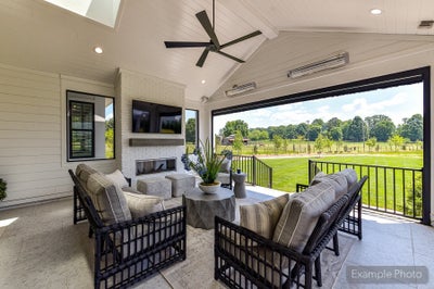 Covered patio with outdoor fireplace, ceiling fan, mounted TV, and seating area overlooking a green backyard