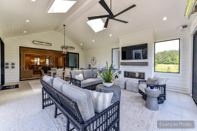 Covered outdoor patio with vaulted ceiling, ceiling fan, fireplace, mounted TV, and wicker seating area