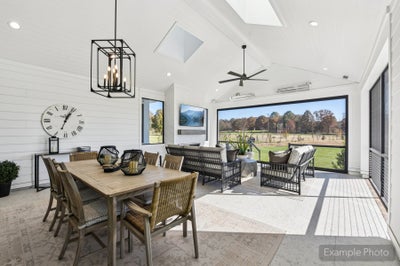 Covered outdoor living area with dining table, seating, ceiling fan, and open views of a grassy yard