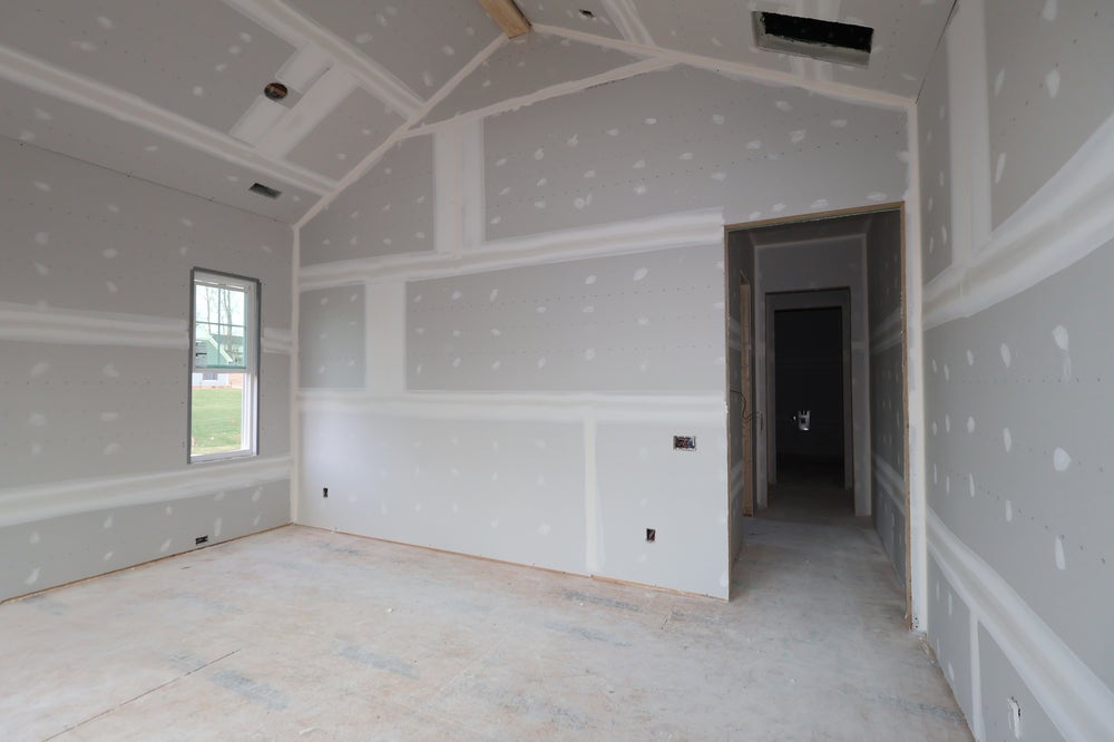 Empty room under construction with drywall, coffered ceiling, and window