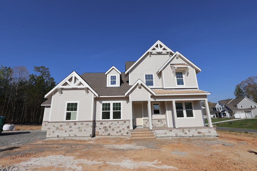 New two-story craftsman home with white siding, stone foundation, and covered front porch under construction