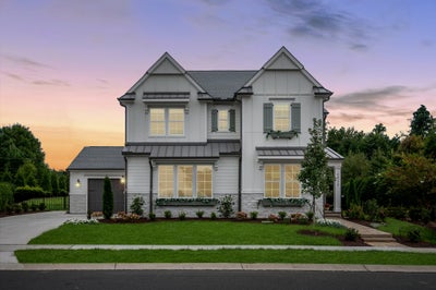 Two-story white farmhouse with board and batten siding, dark shutters, and attached garage at dusk