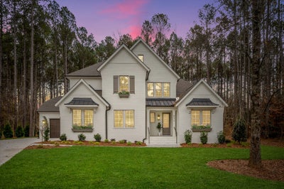 Two-story white brick home with gray shutters and metal roof accents surrounded by pine trees