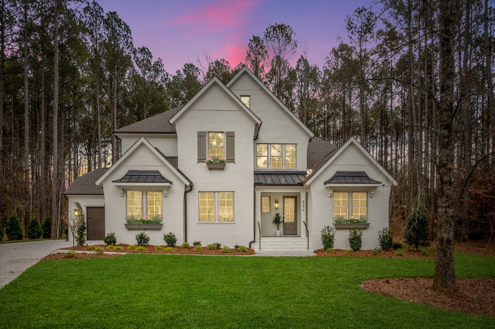 Two-story white brick home with gray shutters and metal roof accents surrounded by pine trees