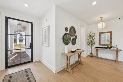 Bright entryway with black-framed glass door, light wood floors, and decorative console tables