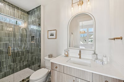 Modern bathroom with green subway tile shower, white vanity, and arched mirror