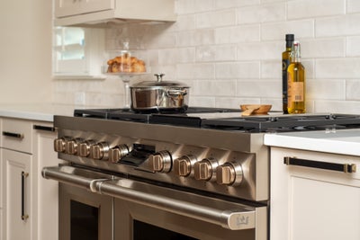 Professional stainless steel gas range with white cabinets and subway tile backsplash