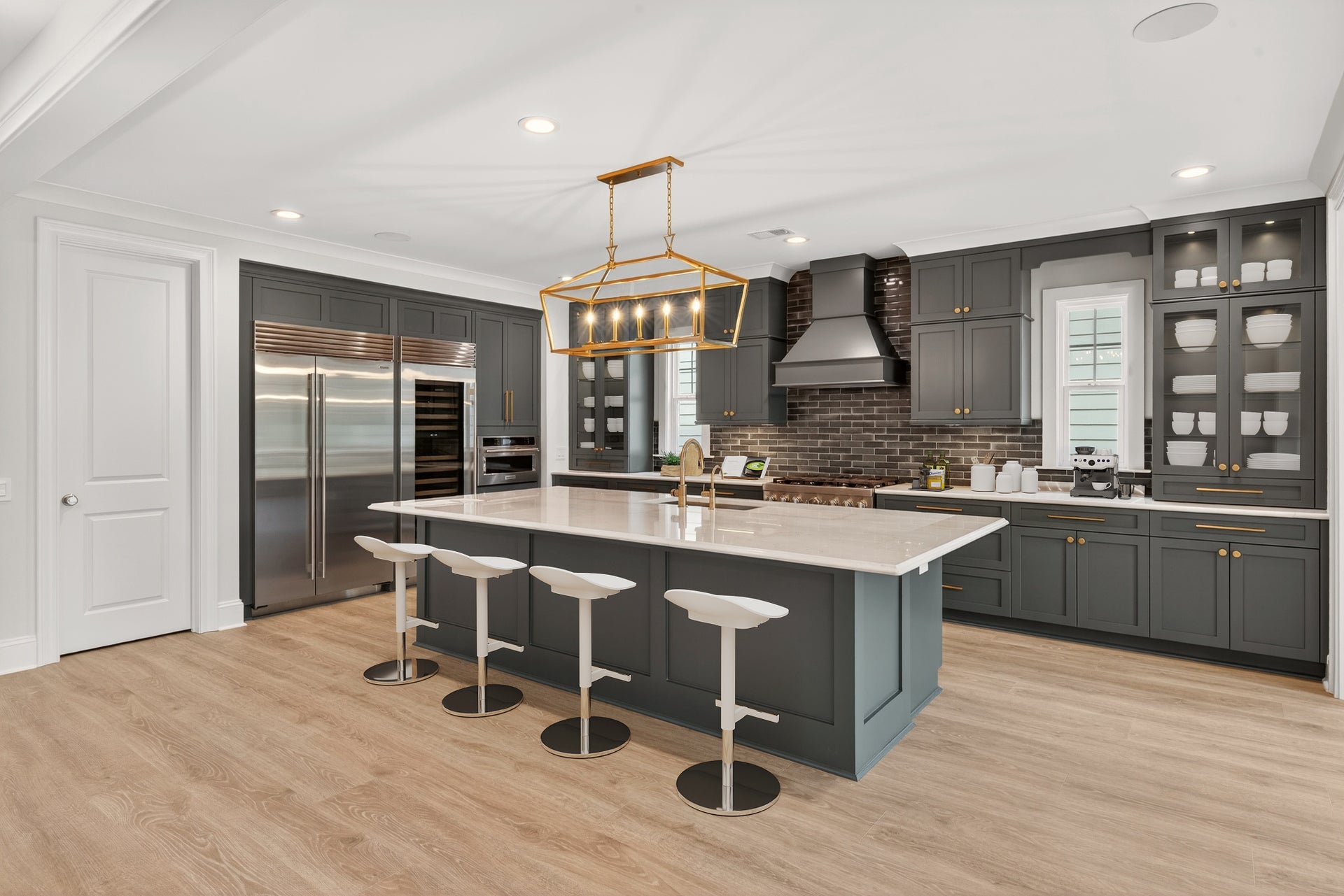 Large kitchen with dark gray cabinets, oversized island with white countertop, four bar stools, and gold pendant light