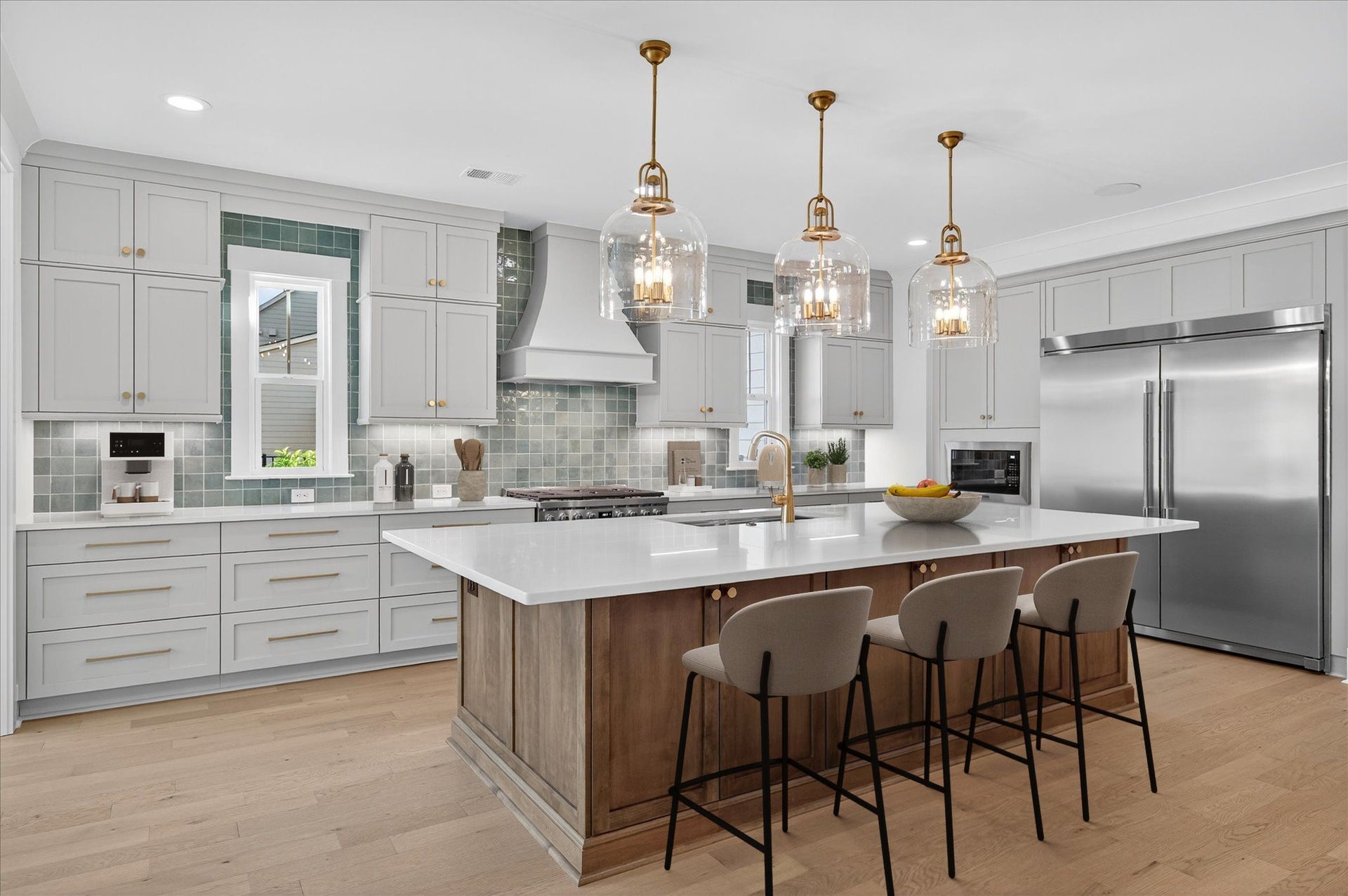Kitchen with gray cabinets, large wood island with bar stools, and three gold pendant lights over white countertops