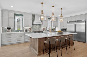Kitchen with gray cabinets, large wood island with bar stools, and three gold pendant lights over white countertops