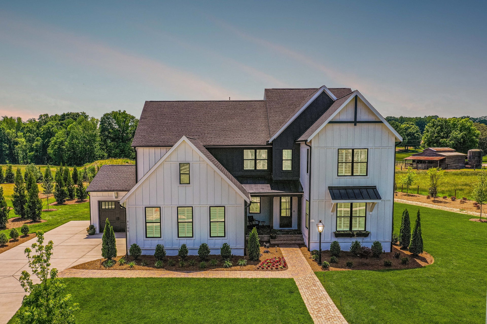 Two-story modern farmhouse with white board-and-batten siding, dark accents, covered porch, and landscaped front yard