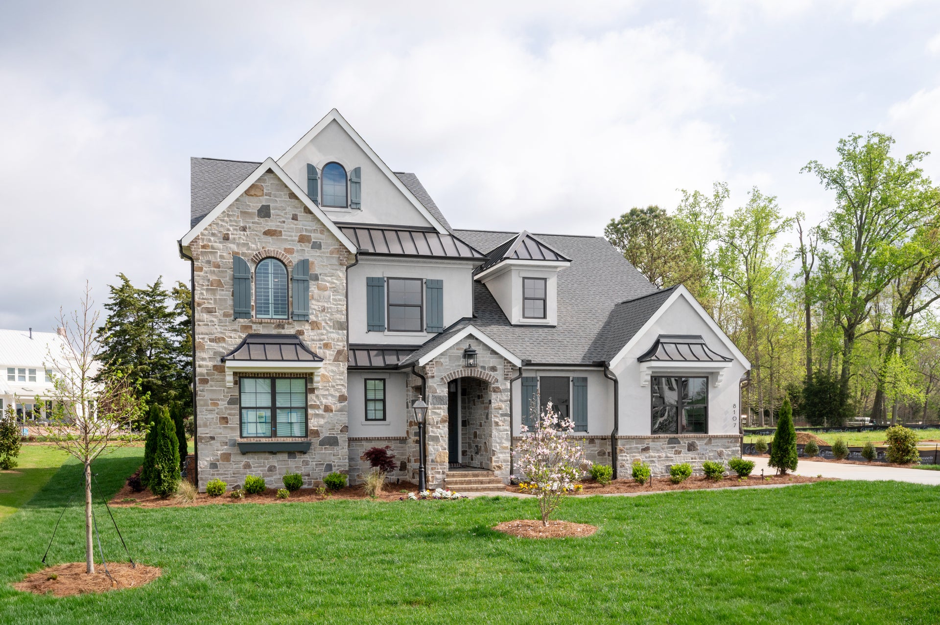 Two-story home with stone and white stucco exterior, metal roof accents, arched entry, and landscaped front yard