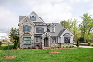 Two-story home with stone and white stucco exterior, metal roof accents, arched entry, and landscaped front yard