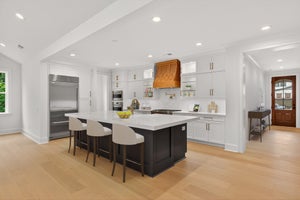 Open kitchen with white cabinets, dark island with bar seating, copper range hood, and light hardwood floors