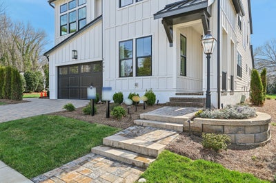 Modern farmhouse exterior with white board-and-batten siding, dark garage door, stone walkway, and landscaped front yard