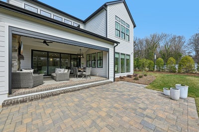 Back of white farmhouse-style home with covered patio, wicker furniture, and brick paver outdoor space