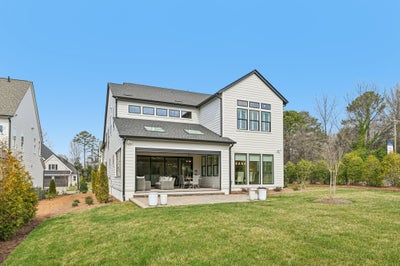 Two-story white home with black trim, rear patio with seating, and green backyard lawn