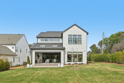Two-story white home with large rear windows, covered patio with seating, and open backyard lawn
